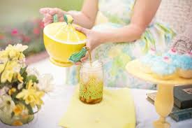 Lady pouring tea from a yellow and green ceramic tea kettle into a tall glass with ice
